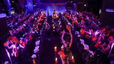 Overhead image of participants on stationary bikes waving pompoms and cycling at of a Cycle for Survival event. 