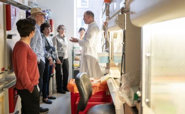 A group of Elizabeth Hamilton Cullum Society members engaged in a discussion with a scientist in a laboratory at MSK. 