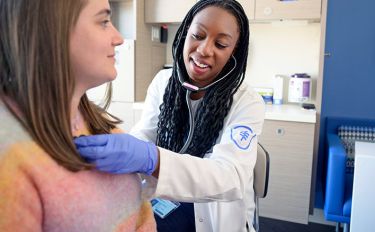 An MSK clinician smiles as she holds a stethoscope to a patient’s chest. 