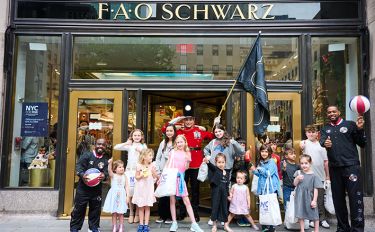 14 children standing outside the entrance of FAO Schwarz in New York City with two members of the Harlem Globetrotters and an FAO Schwarz Toy Solider at the NYC for MSK kickoff breakfast.  
