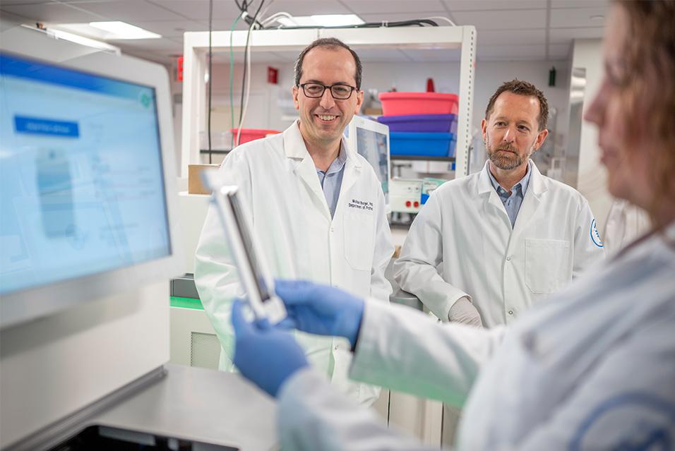 Three MSK staff members stand in a lab, looking at a computer monitor.