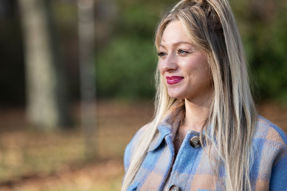 MSK patient Kelly, who was part of the groundbreaking immunotherapy clinical trial, stands outdoors wearing a blue and brown plaid jacket.  