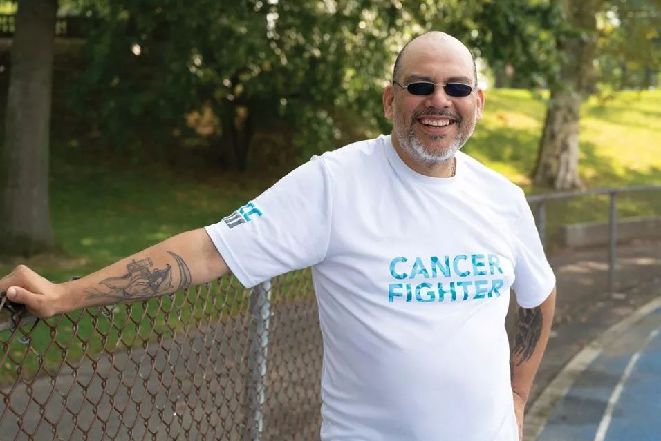 MSK melanoma patient Roberto stands on a blue track wearing a white T-shirt that says “cancer fighter” in blue lettering. 