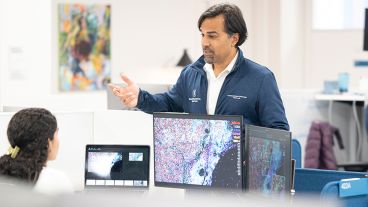 Dr. Sohrab Shah speaks to an MSK staff member who is sitting in front of a computer monitor displaying an image of cells. 