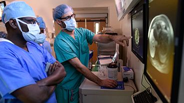 Doctors in scrubs examining medical scans on monitors.