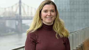 Meredith standing on an outdoor terrace with the 59th Street Bridge in New York City behind her. 