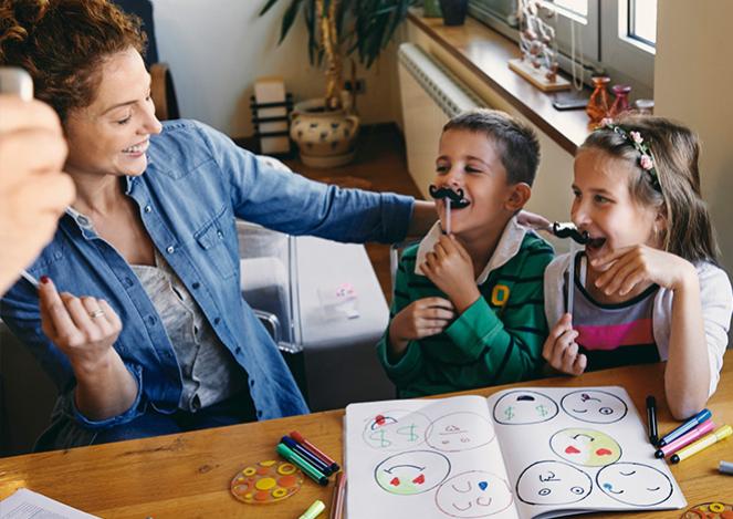  A woman smiles at two laughing children who are holding paper mustaches. 